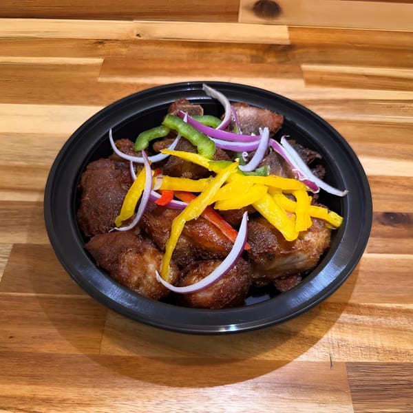 Haitian fried pork (griot) with colorful bell peppers and red onions in a black bowl.