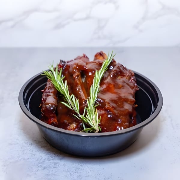 Haitian BBQ ribs with a rich sauce and rosemary sprigs in a black bowl.
