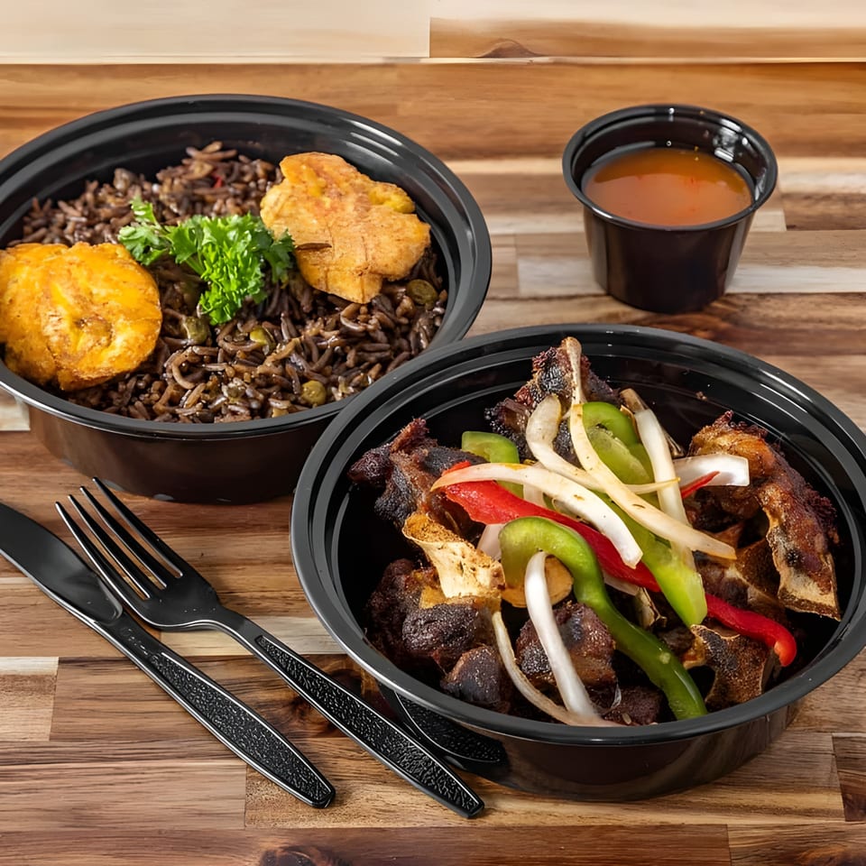 Two Haitian meals in black bowls: rice and plantains, and meat with peppers and onions.