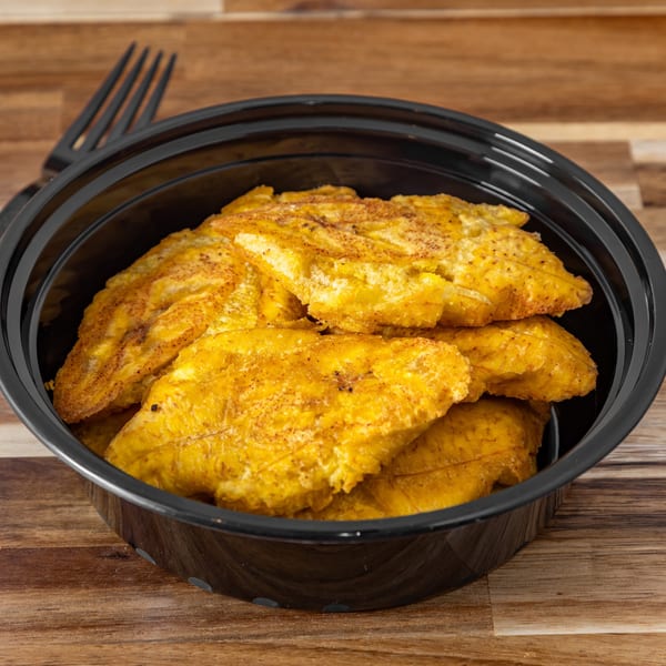 Golden fried plantains, sprinkled with seasoning, in a black bowl on a wooden table.
