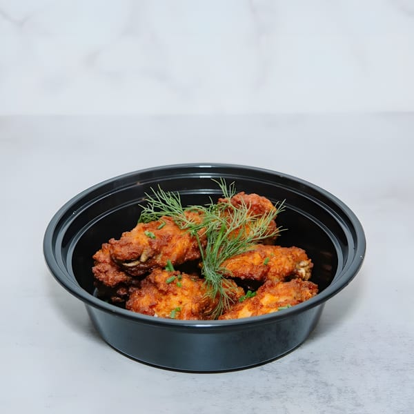 Crispy fried chicken wings garnished with fresh dill and chives in a black takeout container.
