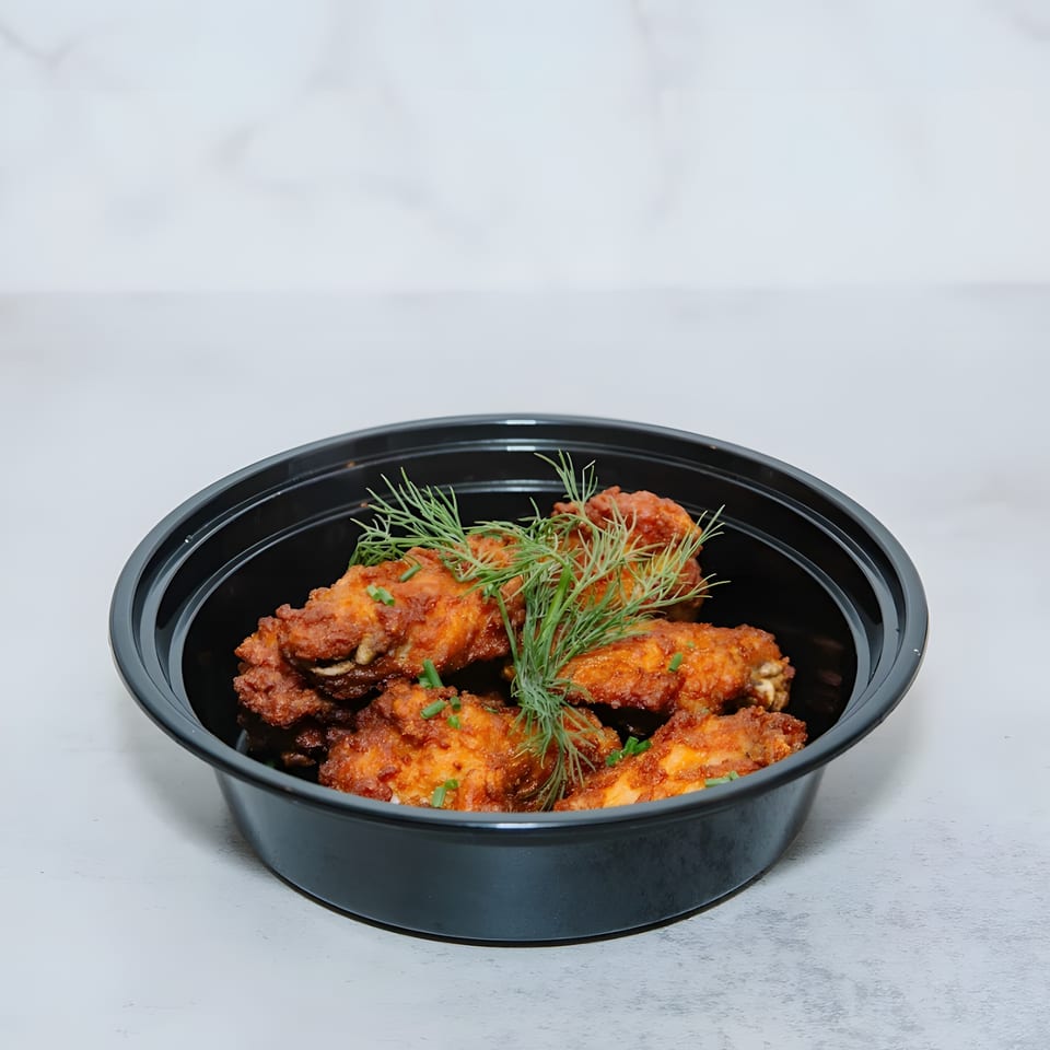Crispy fried chicken wings garnished with fresh dill and chives in a black takeout container.
