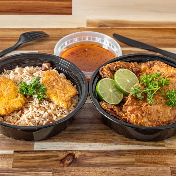 Two Haitian meals in black containers, one with rice and plantains, the other with fried chicken and limes.