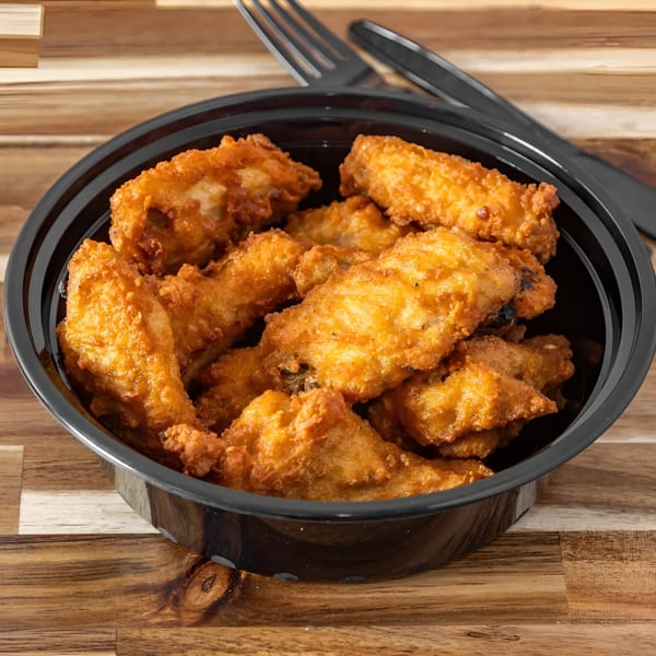 Golden-brown fried chicken pieces in a black bowl, with a fork and knife on a wooden table.