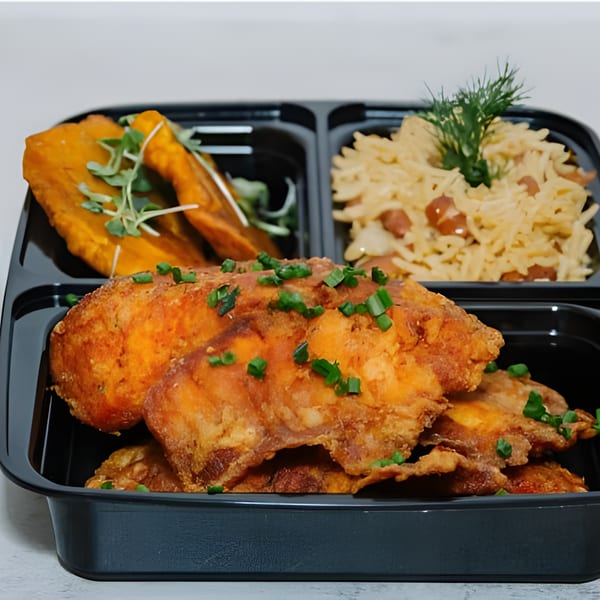 Lakay Buffet's Haitian meal with fried chicken, plantains, and rice in a black to-go container.
